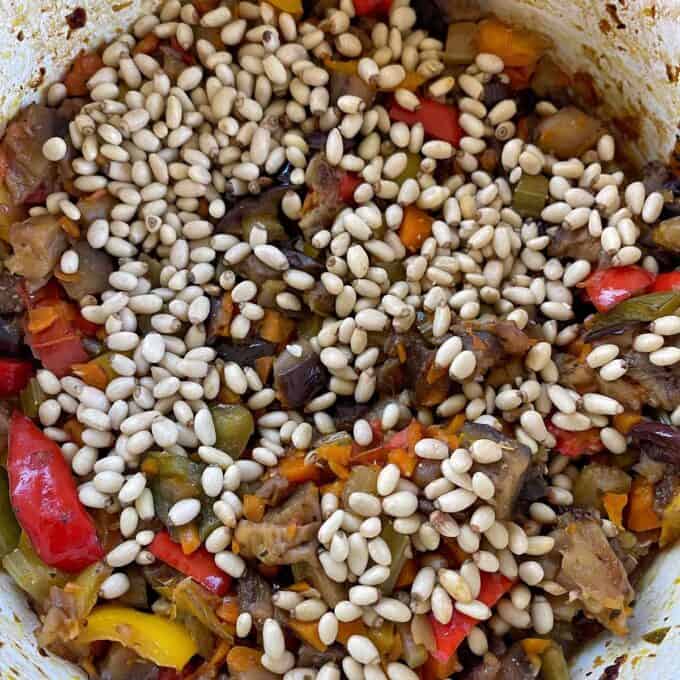 Caponata A close-up of a vegetable stew with chopped peppers and eggplant, topped with a handful of uncooked pine nuts.