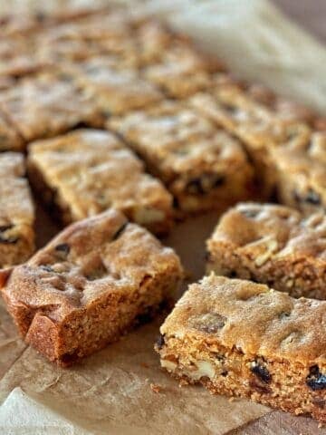 Sliced blondie dessert bars with visible chunks of nuts and chocolate chips, arranged on parchment paper.