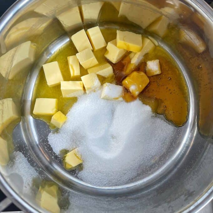 Golden Syrup Sultana Chews Cubed butter, granulated sugar, and a drizzle of honey in a stainless steel pot, ready to be melted or mixed.