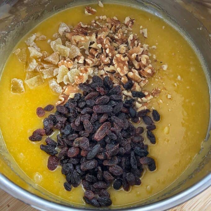 Golden Syrup Sultana Chews A mixing bowl containing batter with chopped walnuts, raisins, and pieces of crystallized ginger on top, ready to be mixed in.