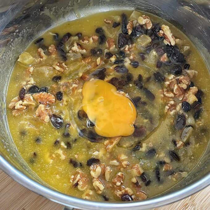 Golden Syrup Sultana Chews A mixing bowl containing egg yolk, chopped walnuts, raisins, black beans, and a yellow liquid mixture.