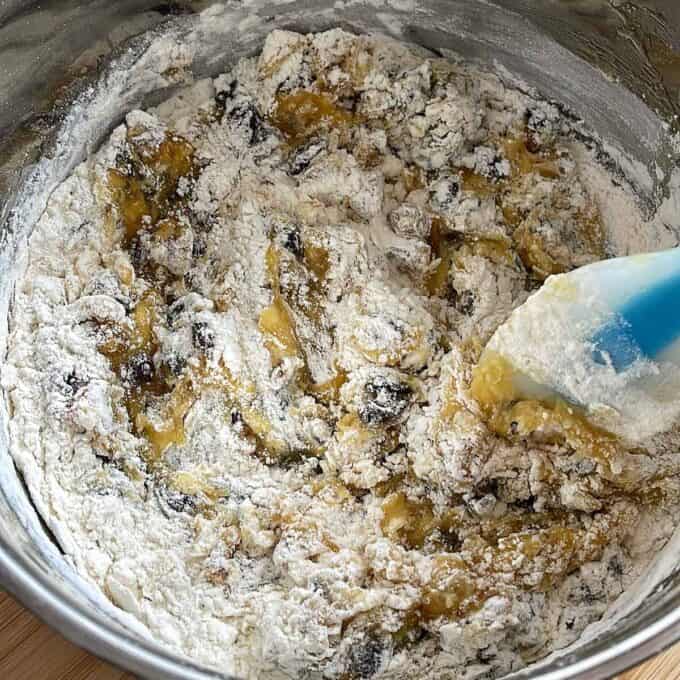 Golden Syrup Sultana Chews A mixing bowl with flour, mashed bananas, and other ingredients being stirred with a silicone spatula, preparing banana bread batter.