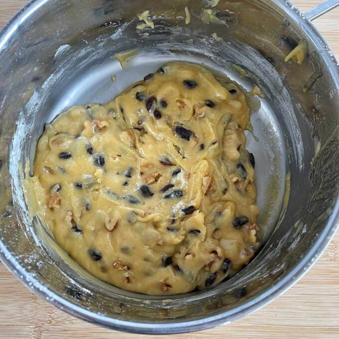Golden Syrup Sultana Chews A mixing bowl containing thick cookie dough with visible chocolate chips and walnut pieces on a wooden surface.