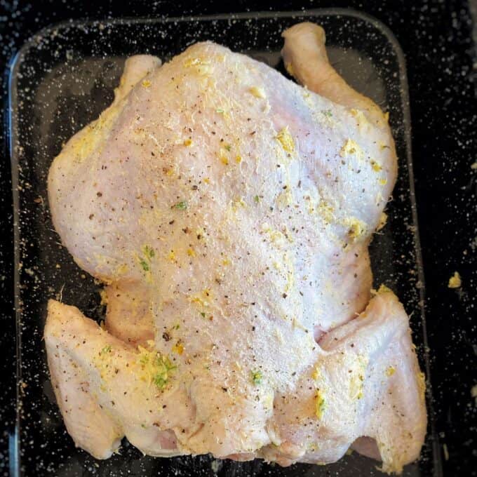 Lemon Garlic Butter Roast Chicken Raw whole chicken seasoned with spices, lemon zest, and herbs, placed in a glass baking dish, ready for cooking.