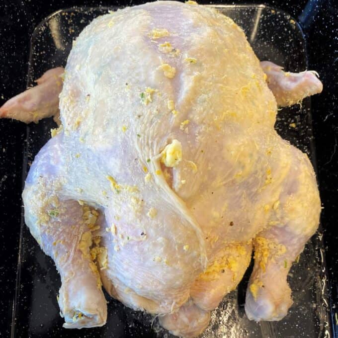 Lemon Garlic Butter Roast Chicken Whole raw chicken seasoned with herbs and butter, placed in a black roasting pan, ready for cooking.