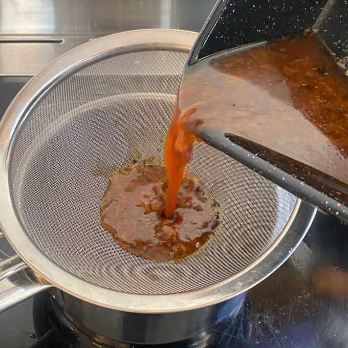 Lemon Garlic Butter Roast Chicken A brown sauce is being poured through a fine mesh strainer into a saucepan on a stovetop.