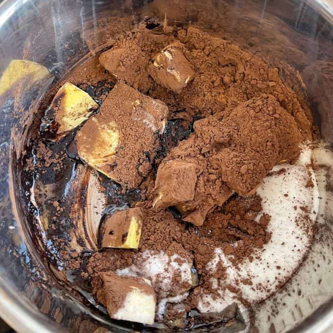 Nanaimo Slice Butter, cocoa powder, sugar, and chocolate are combined in a metal mixing bowl, ready to be melted or blended together.
