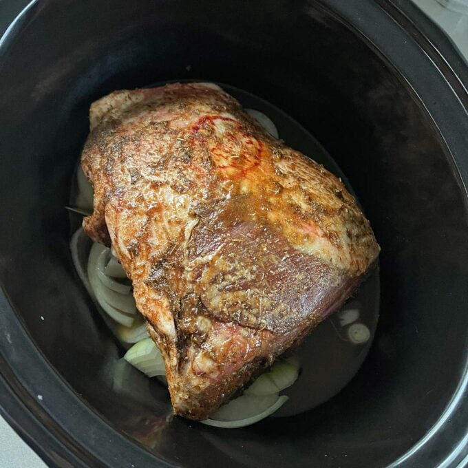 Slow Cooker Lamb Shoulder A seasoned roast sits on sliced onions inside a slow cooker, ready to be cooked.