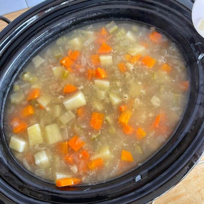 Vegetable Soup A slow cooker filled with vegetable soup, containing chopped carrots, potatoes, and celery in a clear broth.
