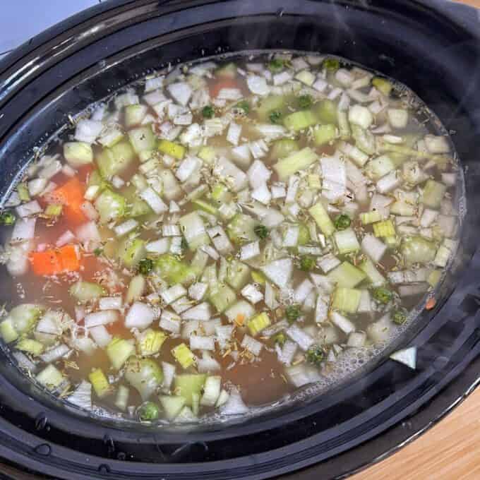 Vegetable Soup A slow cooker filled with chopped onions, celery, carrots, and herbs simmering in broth.