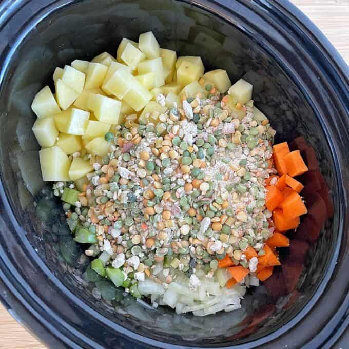 Vegetable Soup Chopped potatoes, carrots, celery, onions, and dry split peas are arranged in sections inside a black slow cooker.