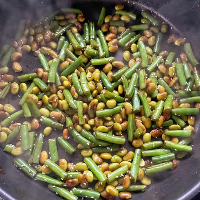 Sesame Chicken Rice Bowls Green beans and edamame sautéed in a pan with sesame seeds.