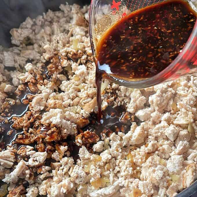 Sesame Chicken Rice Bowls Ground meat is being cooked in a pan while a dark sauce is poured over it from a measuring cup.