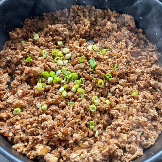 Sesame Chicken Rice Bowls Cooked ground meat topped with chopped green onions in a pan.