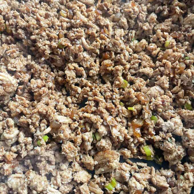 Sesame Chicken Rice Bowls Cooked ground meat mixed with diced vegetables and seasonings in a pan.