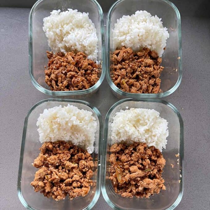 Sesame Chicken Rice Bowls Four glass meal prep containers each hold a serving of white rice and cooked ground meat, arranged side by side on a gray surface.