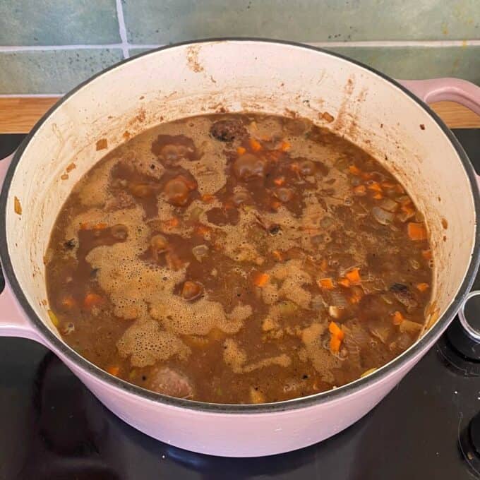 Steak and Cheese Pie A pot of brown stew with visible chunks of meat, carrots, and onions simmers on a stovetop.