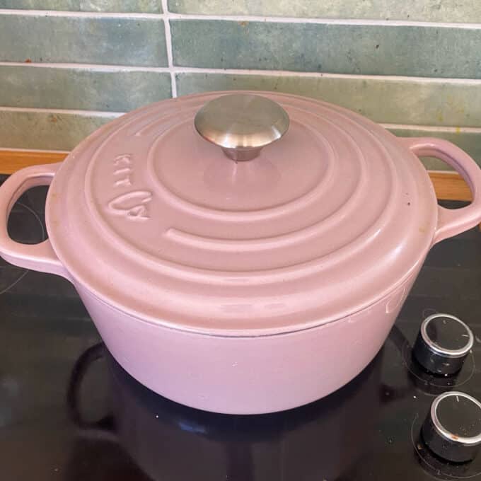 Steak and Cheese Pie A pink Dutch oven with a metal handle sits on a black stovetop in front of a green tiled backsplash.