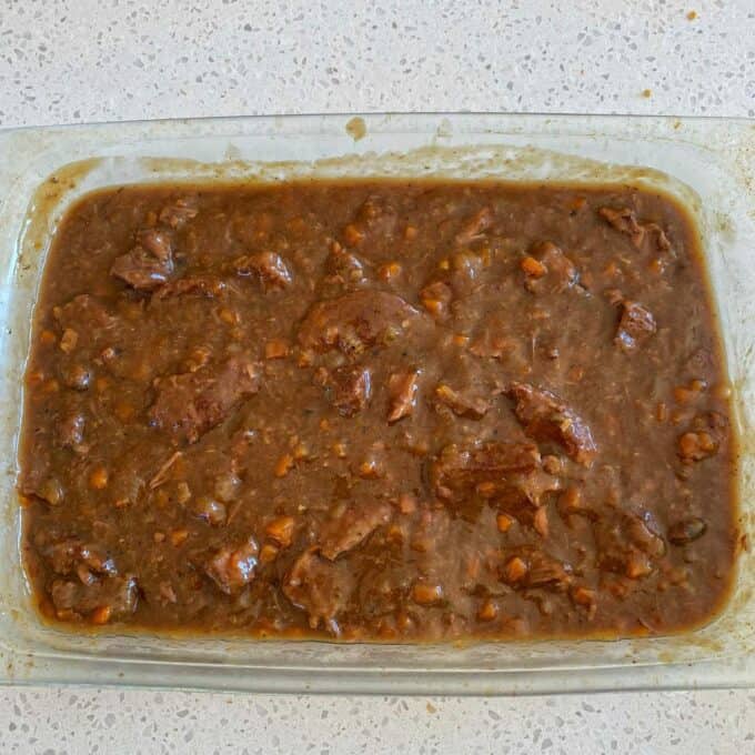 Steak and Cheese Pie A glass dish filled with beef stew in a thick brown gravy, containing chunks of meat and diced vegetables, on a speckled countertop.