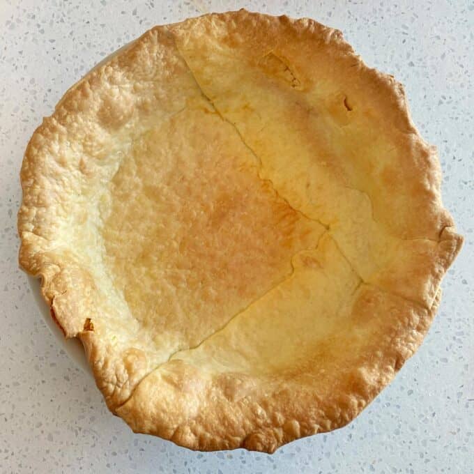 Steak and Cheese Pie A baked pie crust with no filling, showing a golden brown, slightly cracked surface, in a white dish on a speckled countertop.