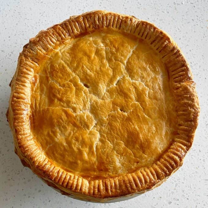 Steak and Cheese Pie A round, golden-brown pie with a flaky, crimped crust sits on a speckled white countertop.