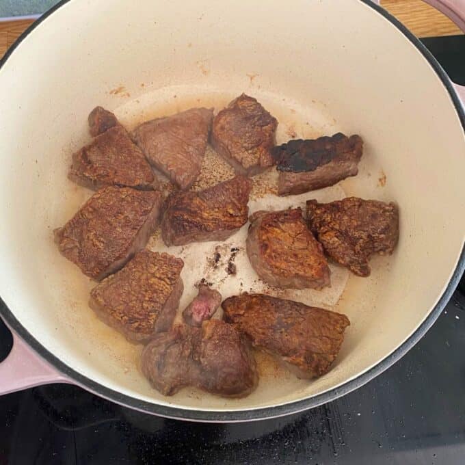Steak and Cheese Pie Chunks of beef searing in a large white pot on a stovetop, with some pieces browned and a few bits stuck to the bottom.