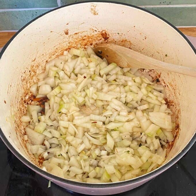 Steak and Cheese Pie Chopped onions cooking in a large pot with browned residue and a wooden spoon.
