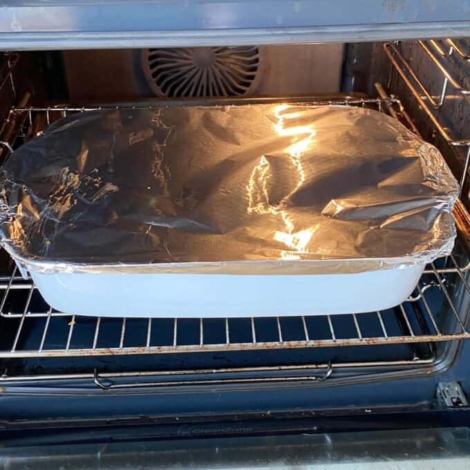 Chicken Tikka Tray Bake A white baking dish covered with aluminum foil is placed on the middle rack inside an oven.