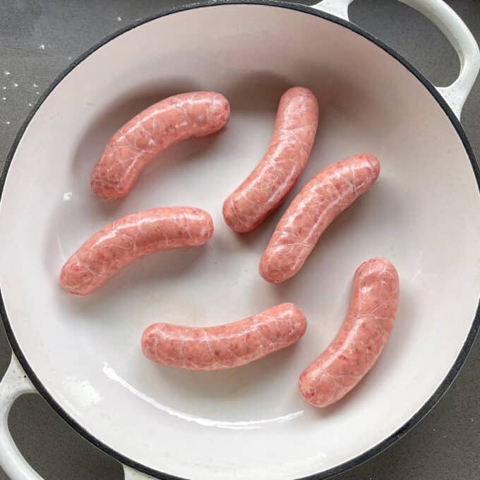Toad in the Hole Five raw sausages arranged in a white enameled cast iron pan.