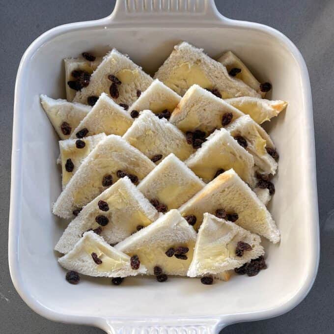 Bread and Butter Pudding Slices of white bread with butter and raisins arranged in a white ceramic baking dish.