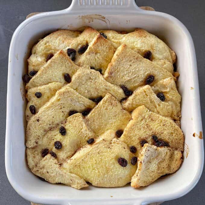 Bread and Butter Pudding A baked bread pudding in a white dish, featuring golden bread slices and scattered raisins on top.