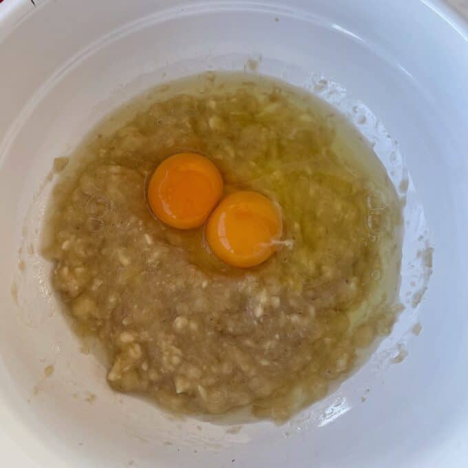 Banana and Raspberry Baked Oats Two raw eggs sit on top of mashed bananas in a white mixing bowl.