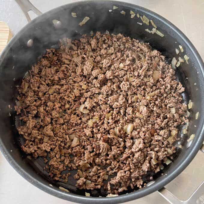 Hash Bite Burger Bowls Ground beef and diced onions cooking in a black skillet on a stovetop.