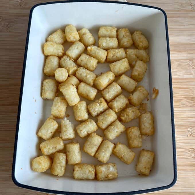 Hash Bite Burger Bowls Rectangular baking dish filled with golden brown tater tots arranged in a single layer on a wooden surface.