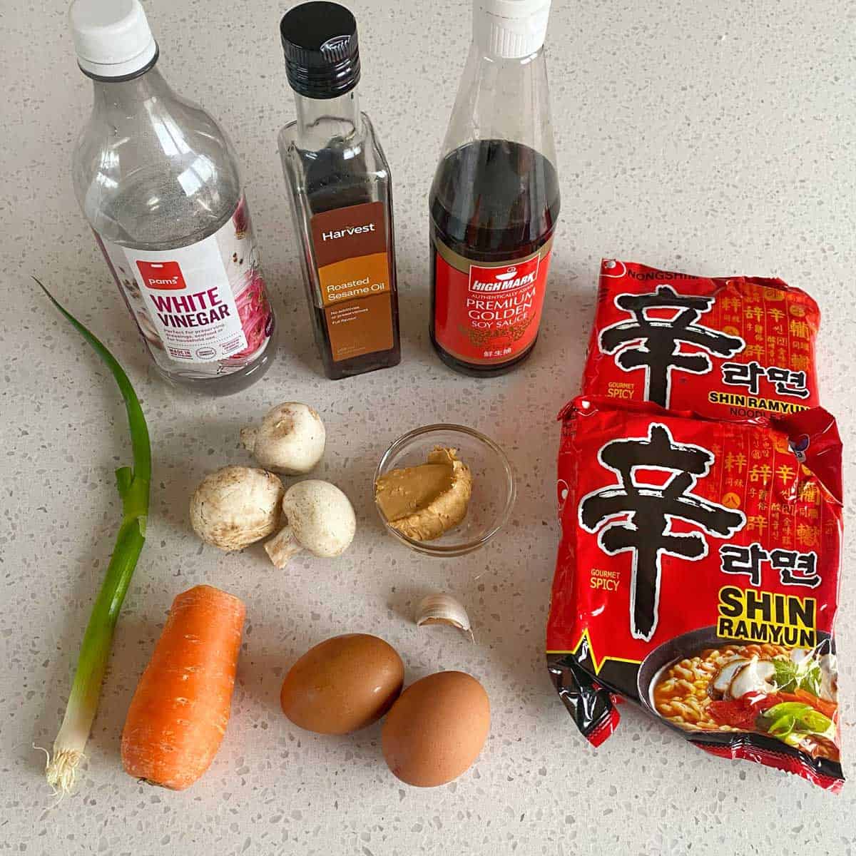 Spicy Ramen and Egg Assorted ingredients on a countertop include white vinegar, roasted sesame oil, soy sauce, instant ramen, a carrot, green onion, mushrooms, garlic, eggs, and miso paste.