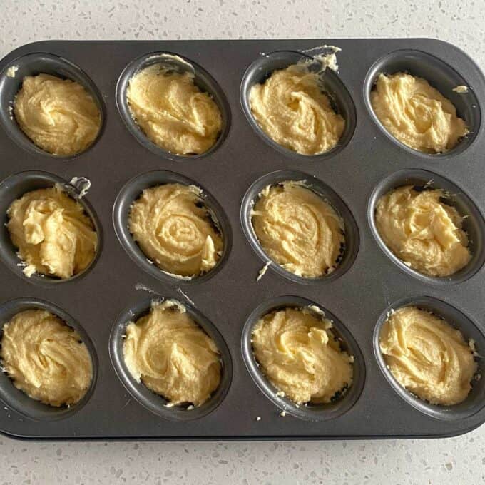 Raspberry Friands A muffin tray filled with unbaked muffin batter sitting on a light-colored countertop.