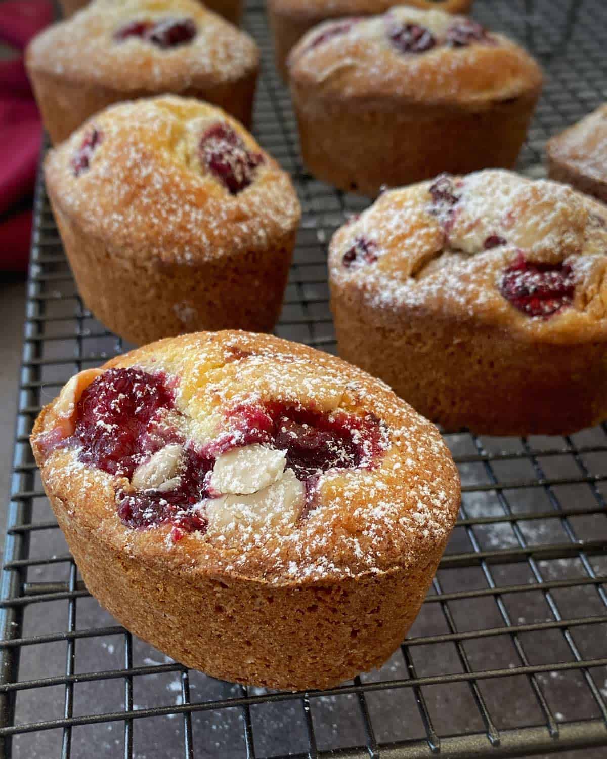Close-up of several raspberry muffins dusted with powdered sugar, cooling on a wire rack.