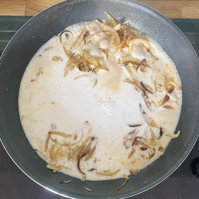 Thai Green Curry Kumara Gratin A frying pan containing sliced onions cooking in a creamy liquid, possibly milk or cream, on a stovetop.