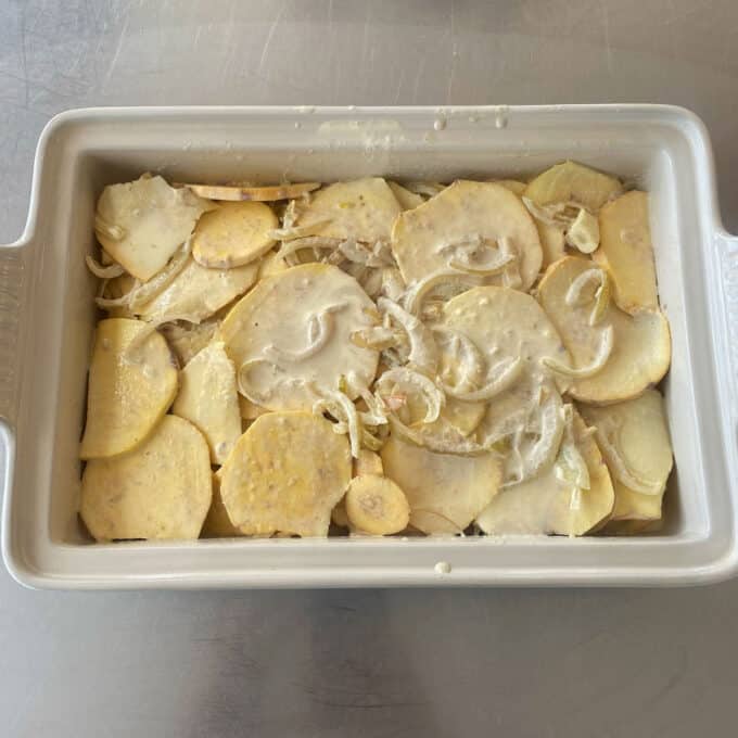 Thai Green Curry Kumara Gratin A rectangular baking dish filled with sliced potatoes and onions coated in a creamy sauce, ready for baking.
