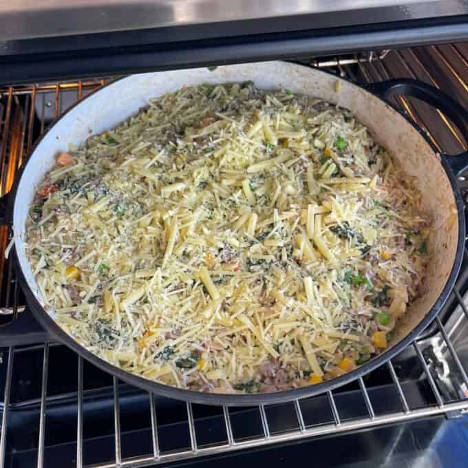 Large skillet with mixed rice, vegetables, and shredded cheese on top, placed on an oven rack for baking.