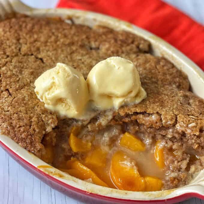 Peach Cobbler A peach cobbler topped with two scoops of vanilla ice cream, with a portion scooped out to reveal the filling.