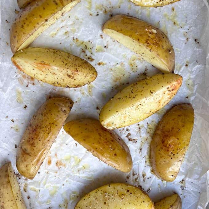 Pork Souvlaki Tray Bake Potato wedges seasoned with pepper and salt on a parchment-lined baking sheet, ready for roasting.
