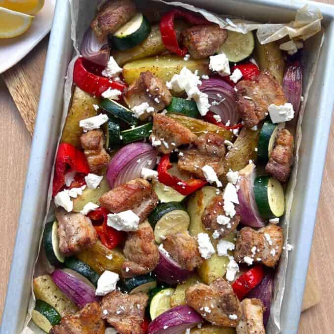 Pork Souvlaki Tray Bake A sheet pan with roasted pork pieces, zucchini, red bell pepper, red onion, and potato slices, topped with crumbled feta cheese.