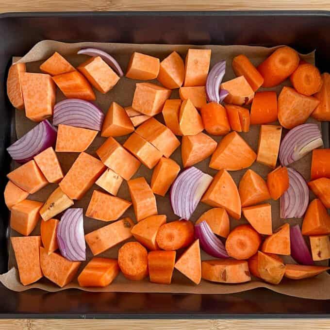 Quinoa, Kumara and Carrot Salad Chopped sweet potatoes, carrots, and red onions are arranged on a parchment-lined baking tray, ready for roasting.