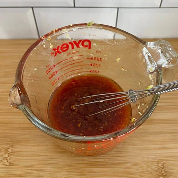 Quinoa, Kumara and Carrot Salad A glass measuring cup with red liquid sauce and a small whisk inside sits on a wooden surface.