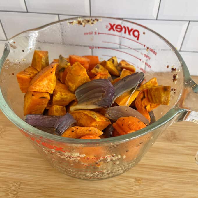 Quinoa, Kumara and Carrot Salad Roasted sweet potatoes, carrots, and red onions in a glass Pyrex measuring cup on a wooden surface.