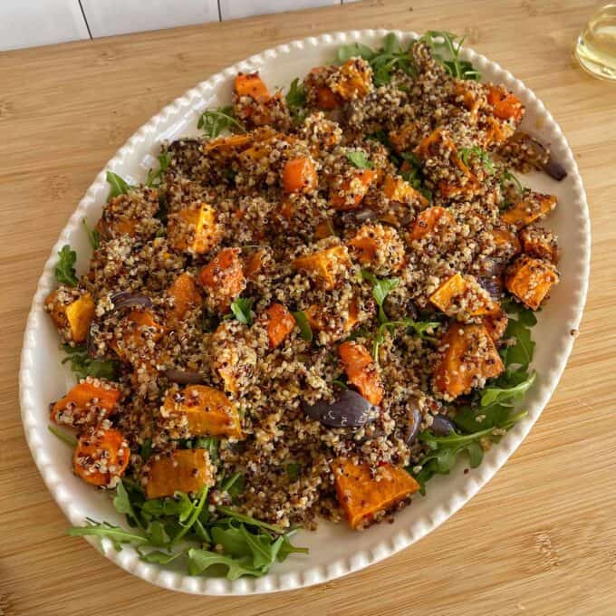 Quinoa, Kumara and Carrot Salad A platter of quinoa salad with roasted sweet potatoes, red onions, and arugula on a wooden table.