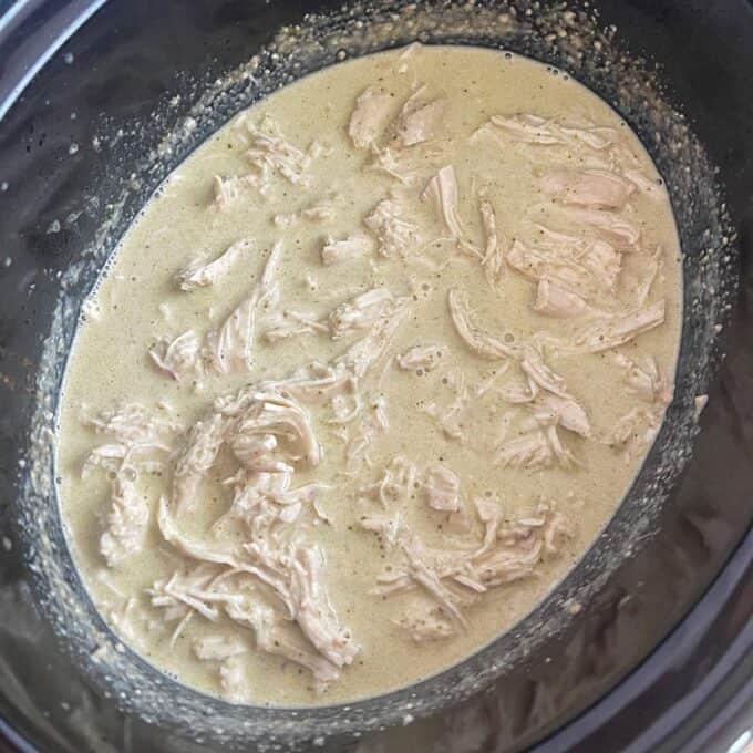 Shredded chicken in a creamy sauce inside a slow cooker.