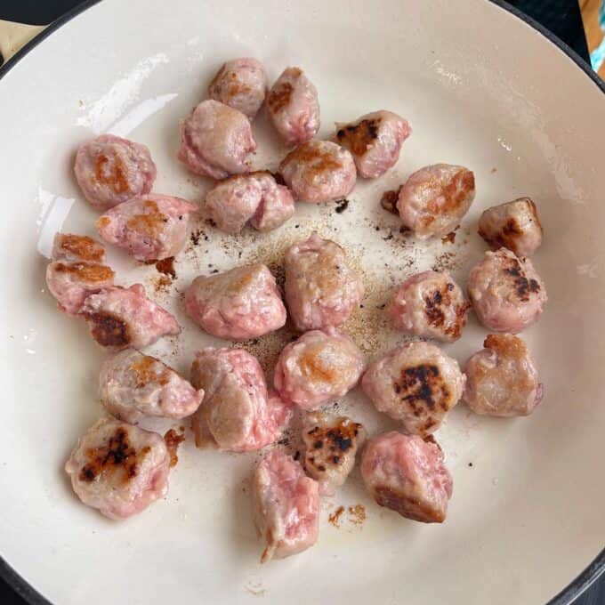 Satay Sausage Rice Bowl Chunks of partially browned meat cooking in a white frying pan.