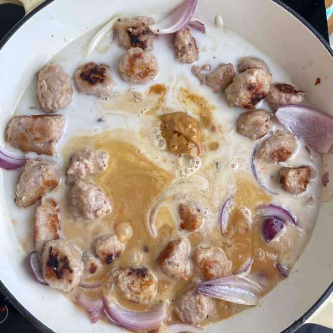 Satay Sausage Rice Bowl Chunks of browned meat, sliced red onions, and a dollop of paste are simmering in a creamy liquid inside a white pan.